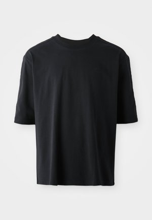 Juodas trumpas rankovėmis marškinėliai, pagaminti iš minkštos medvilnės, su apvaliu kaklu ir subtiliu logotipu priekyje. Lygi tekstūra ir laisvas siluetas.