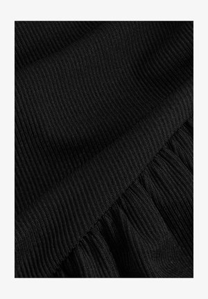 Tessuto a coste nero con una superficie liscia nella parte superiore, che si trasforma in una sezione arricciata e texturizzata nella parte inferiore.