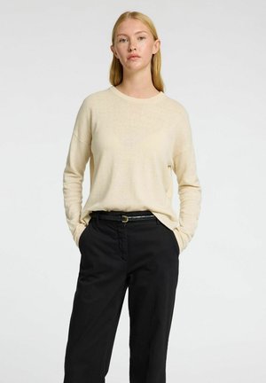 Beige langærmet sweater med en afslappet pasform, parret med sorte bukser og et sort bælte, der har et enkelt design og en blød tekstur.