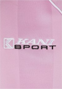 Light pink sportswear featuring a textured fabric. The logo "KANI SPORT" is embroidered, with "KANI" in white and "SPORT" in black.