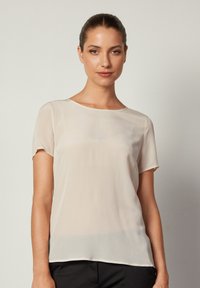 Beige, kortärmad blus i ett lätt, genomskinligt tyg. Har en rund halsringning och en subtil fåll som ger en avslappnad passform.