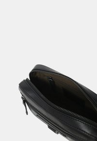  Pochette nera in pelle con chiusura a zip. Presenta un esterno liscio, cuciture a contrasto e un ampio interno beige.