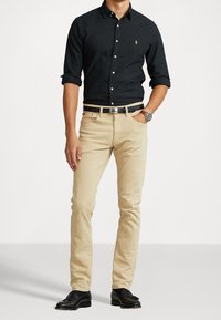 Czarna koszula zapinana na guziki, beżowe slim-fit spodnie, czarny pasek i czarne buty. Klasyczny design z logo polo na koszuli.