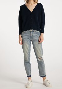 Granatowy prążkowany kardigan z dekoltem w serek, ozdobiony drewnianymi guzikami i długimi rękawami, zestawiony z jasnoniebieskimi, przetartymi jeansami i białymi trampkami.