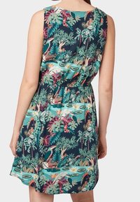 Ärmlös, knälång klänning i mörk teal-tyg med ett tropiskt mönster som har palmblad, flamingos och olika färgglada mönster.