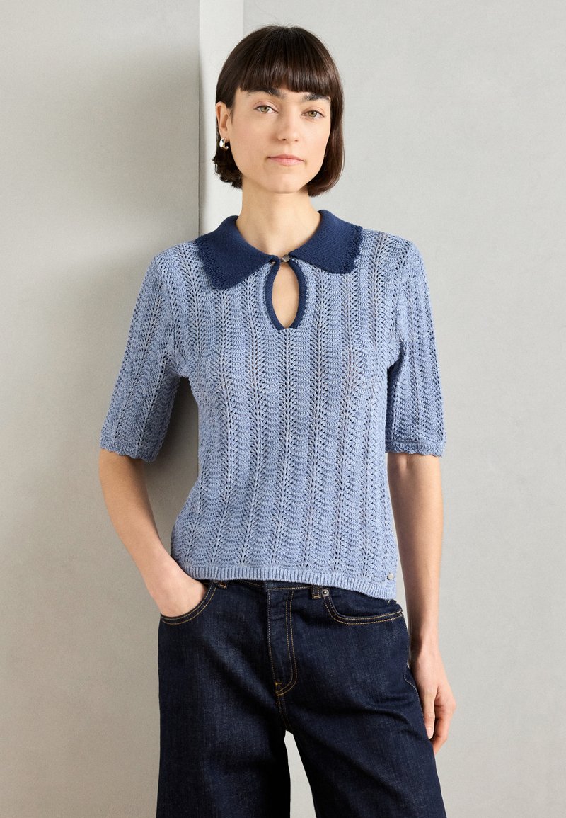 Ανοιχτό μπλε πλεκτό τοπ κοντομάνικο με ναυτική κολάρο, λεπτομέρεια κλειδαρότρυπας και υφασμάτινο σχέδιο. Συνδυασμένο με σκούρες τζην παντελόνες.