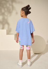 Világoskék, laza szabású póló virágos hímzéssel a hátán, virágmintás leggingssel és fehér magas szárú tornacipőkkel párosítva.