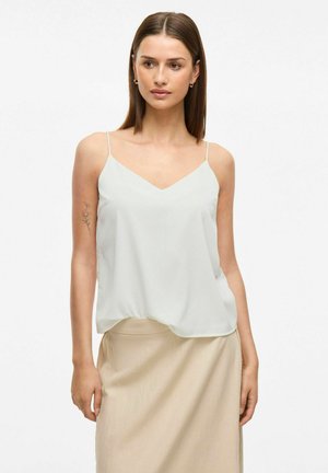 Camiseta sin mangas de corte en v ligera en suave tejido crema con tirantes finos, combinada con una falda beige. Textura suave con una silueta fluida.