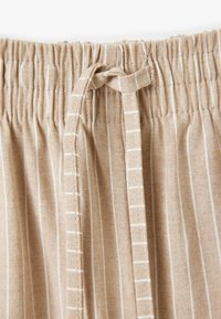 Pantaloni beige a righe con vita elasticizzata e coulisse. Il tessuto ha una trama texturizzata, con sottili righe verticali bianche.
