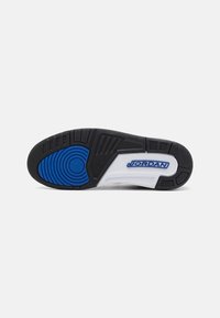 Fekete sneaker külső talp kerek kék akcentussal, texturált mintákkal és egy sima panelen lévő fehér Jordan logóval.
