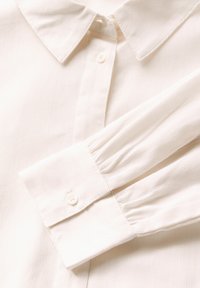 Witte gestreepte blouse met een klassieke kraag, knoopsluiting aan de voorkant en gathered mouwdetails. Gemaakt van lichte stof met een zachte textuur.