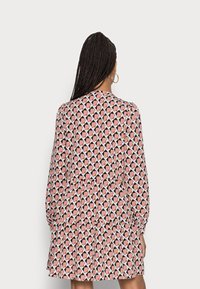 Dlouhý rukáv, vícevrstvé šaty s geometrickým vzorem v růžové, černé a bílé barvě. Mají kulatý výstřih a elastické manžety.