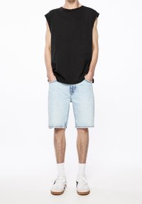 Musta hihaton paita, joka on yhdistetty vaaleansinisiin farkkuhousuihin. Mallilla on päällään valkoiset tennarit, joissa on vaaleat pohjat, sekä valkoiset nilkkasukat.