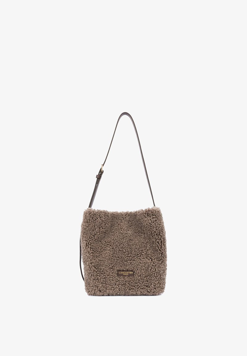 Sac fourre-tout brun duveteux avec une longue sangle réglable et une petite plaque logo dorée "Lancaster Paris" sur le devant.