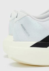 Gros plan de la zone du talon d'une chaussure blanche Adidas Adizero Evo SL avec une semelle blanche épaisse et un accent noir.
