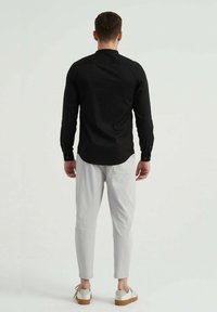 Chemise noire à manches longues avec des poignets à boutons, assortie à un pantalon tapered gris clair et des baskets blanches avec une semelle beige. Design simple, sans motifs.