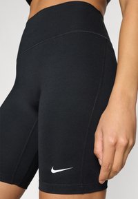 Μαύρο αθλητικό σορτς από ελαστικό ύφασμα, με ψηλή μέση, επίπεδες ραφές και λευκό λογότυπο Nike κοντά στο τελείωμα.