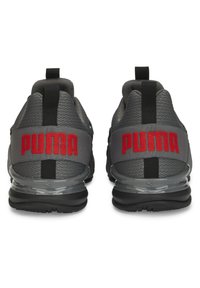 Baskets Puma avec un-dessus en maille grise, des accents noirs et des boucles élastiques au niveau du talon ; logo "PUMA" rouge à l'arrière ; semelle en caoutchouc transparent.
