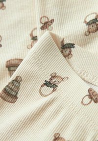 Tissu côtelé en crème avec un motif de singes en peluche marron et de chapeaux décoratifs. Comprend des coutures visibles et une texture douce.