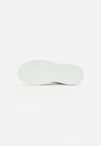 Semelle de chaussure en caoutchouc blanc avec un motif de semelle en forme de hexagone. Bords arrondis et texture lisse, comportant des détails de marque en relief.