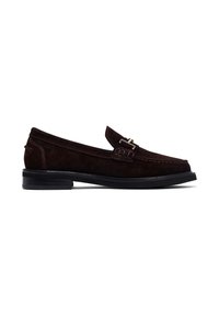 Mocasines de ante marrón con punta redonda, acentos de costura y una hebilla metálica decorativa en el empeine. Suela plana de goma negra.
