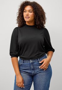 Zwarte, lichte top met een hoge hals en pofmouwen, gecombineerd met high-waisted blauwe jeans. Soepele textuur met een aansluitende silhouette.
