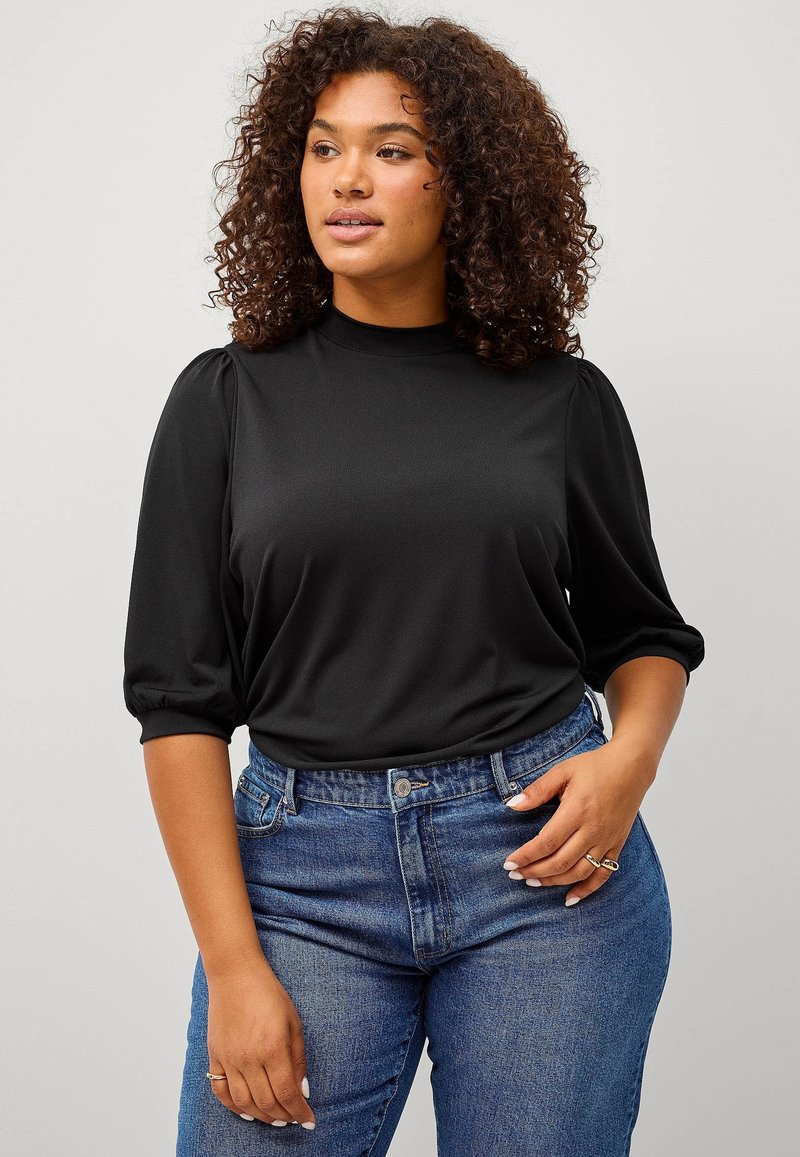 Zwarte, lichte top met een hoge hals en pofmouwen, gecombineerd met high-waisted blauwe jeans. Soepele textuur met een aansluitende silhouette.