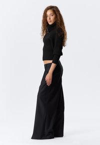 Czarny sweter z golfem w prążki i szerokie czarne spodnie. Sweter ma złożone mankiety; spodnie mają cienkie prążki i boczne kieszenie.