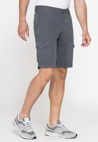 Pantaloni cargo grigi in cotone, con tasche laterali, vestibilità rilassata e taglio dritto. Abbinati a scarpe da ginnastica grigie.