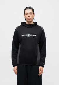 Μαύρο φούτερ Nike Shox με λογότυπο στο εμπρόσθιο μέρος, πλευρικά πάνελ σε πιο σκούρο χρώμα, ενσωματωμένη κουκούλα και ριμπ μανσέτες. Μαλακή υφή υφάσματος.