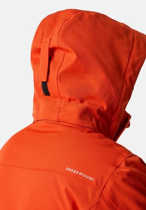 Oranje waterdichte jas met een oprolbare capuchon, beschikt over een zwarte lus en een witte logo-tekst "SWEDEMOUNT" op de schoudernaad.
