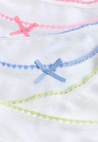 Indumenti in cotone con tessuto bianco decorato con bordi in pizzo colorato. Nastrini decorativi blu, rosa e verdi sono cuciti in un motivo a croce.