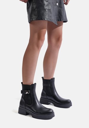 Stivali alla caviglia neri dal design elegante, realizzati in pelle. Presentano una suola spessa, pannelli laterali elastici e una fibbia decorativa sul lato.