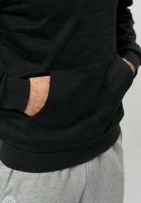 Zwarte sweatshirt met een buidelzak, gestructureerde stof en ribgebreide boorden, gecombineerd met lichtgrijze joggingsbroeken.