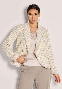 Wit en beige geblokte tweed jasje met rafelige randen, dubbelzijdig ontwerp en zilveren knopaccenten, gedragen over een kanten top.