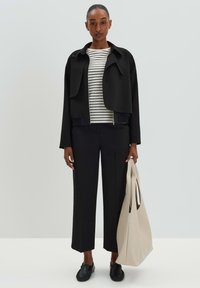 Zwarte cropped jasje over een wit en zwart gestreepte shirt, gecombineerd met zwarte wijde broek en een beige tote bag. Soepele texturen.