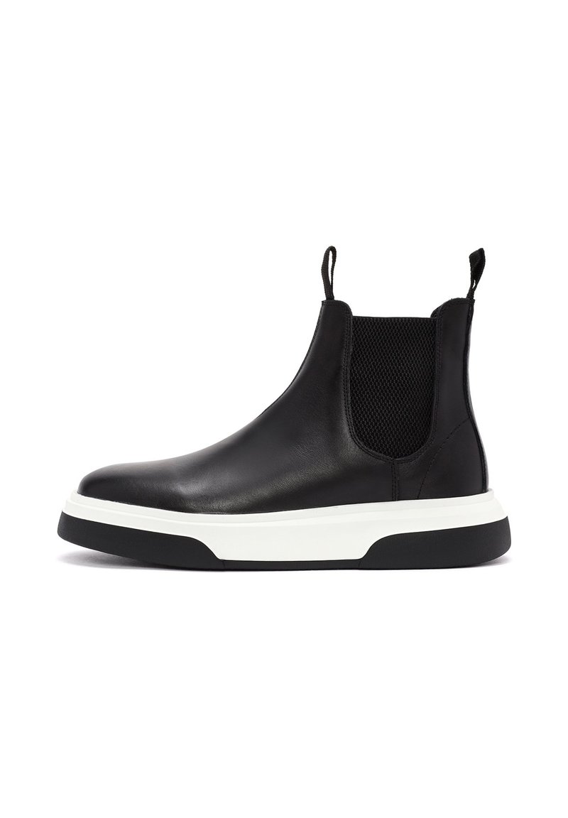 Botín Chelsea de cuero negro con paneles laterales elásticos, suela intermedia blanca y suela exterior negra en contraste. Incluye una lengüeta para facilitar su uso.