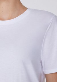 Biała bawełniana koszulka z klasycznym okrągłym dekoltem, krótkimi rękawami i gładką fakturą materiału. Prosty i minimalistyczny design.