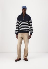 Navy striped fleece pullover with half zipper, beige textured pants, and brown shoes. Wearing a light blue cap. Simple, casual design.