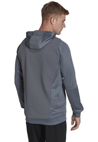 Felpa grigia con cappuccio, caratterizzata da pannelli testurizzati e un tessuto liscio, con maniche lunghe e vestibilità rilassata, adatta per abbigliamento sportivo.