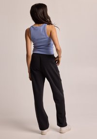 Blue ribbed tank top with black relaxed-fit pants. Pants feature an elastic waistband and a single back pocket. White sneakers complete the look.
