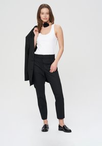 Czarne dopasowane spodnie w połączeniu z białym, prążkowanym topem na ramiączkach, uzupełnione czarną marynarką noszoną na jednym ramieniu. Lśniące czarne mokasyny.