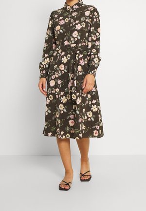Robe fleurie avec un fond brun foncé, ornée de fleurs roses et blanches, manches longues, col et ceinture nouée à la taille. Détail d'ourlet fendu.