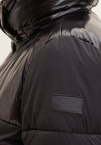 Zbliżenie na ramię błyszczącej czarnej kurtki puchowej z naszywką na tkaninie "DENIM TOM TAILOR".