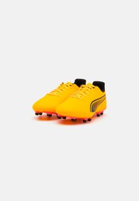 Scarpe da calcio gialle brillanti con una parte superiore testurizzata, accenti neri e tacchetti di colore rosa. Presentano lacci e un design a scollo basso.