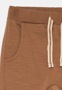 Brune, teksturert stoff joggebukse med ribbestrikket midje, som har en snor med beige striper og sidelommer.
