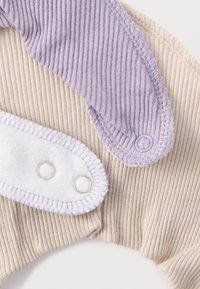 Bawełniany ubranko dla niemowląt w beżowym i jasnofioletowym kolorze. Prążkowana tkanina o fakturze z miękkim białym fragmentem wyposażonym w dwa metalowe zatrzaski i haftowane brzegi.