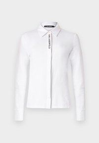 White long-sleeve shirt in cotton with a collared neckline, featuring a vertical black logo on the front and buttoned cuffs.