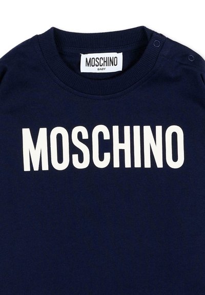 Granatowy niemowlęcy t-shirt z białym logo MOSCHINO na piersi oraz dwoma zatrzaskami na ramieniu przy kołnierzu.
