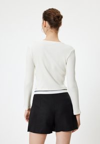 Top de manga larga blanco con canalé y cuello redondo, combinado con pantalones cortos negros que presentan una cinturilla blanca y un dobladillo con forma de escallola.